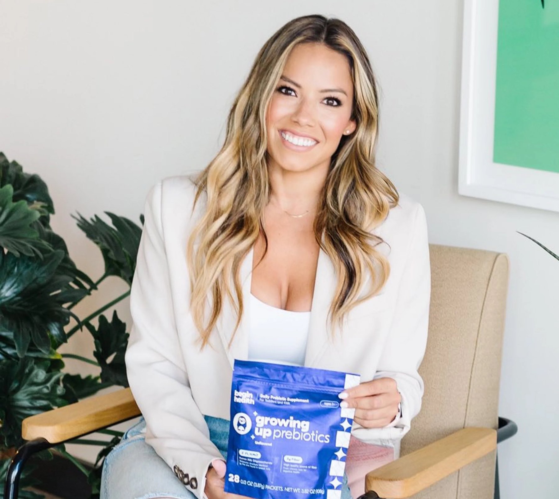 A woman in a chair displays a Begin Health prebiotics packet.