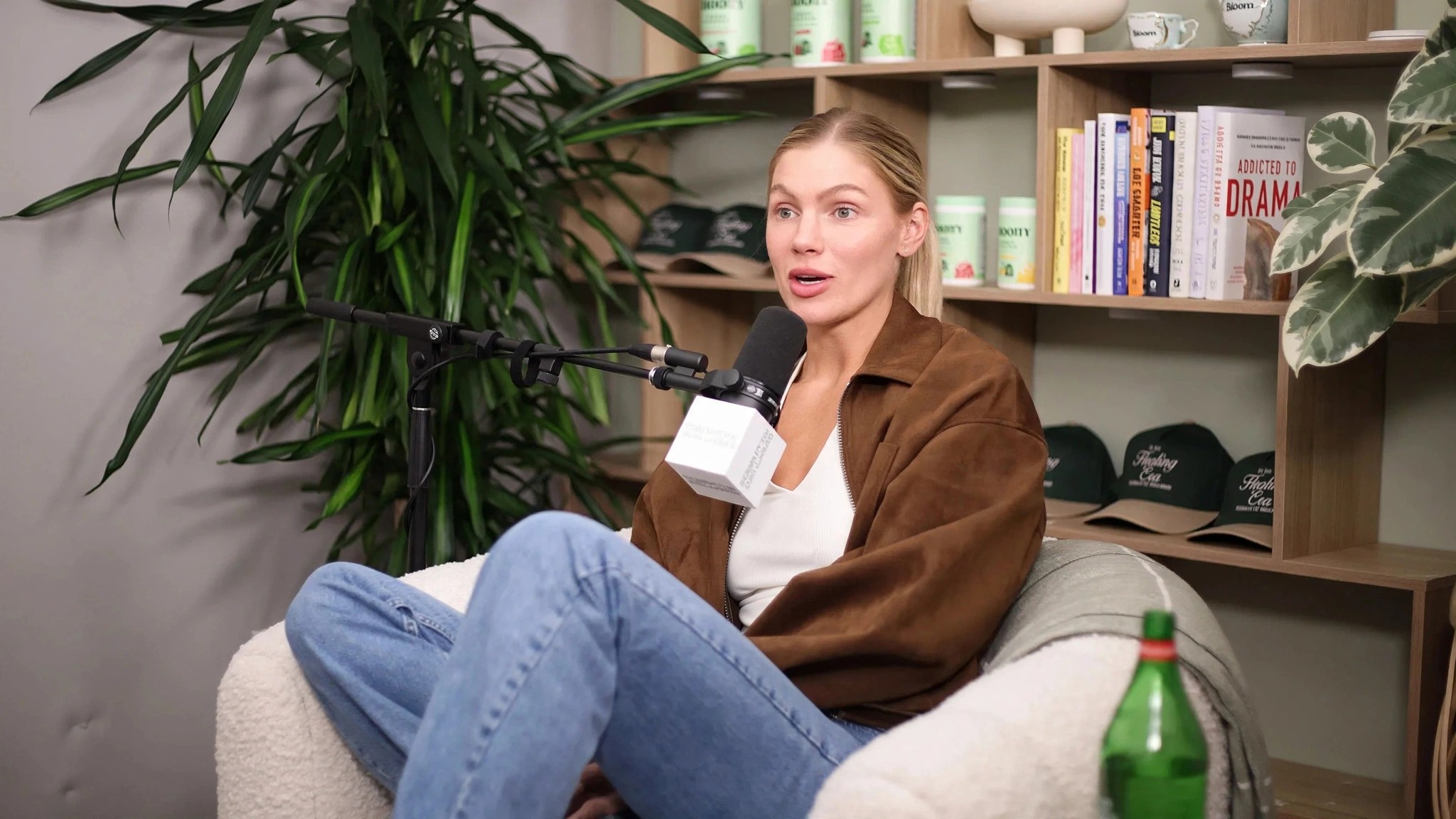 A blonde guest relaxes in a chair holding papers and a microphone.