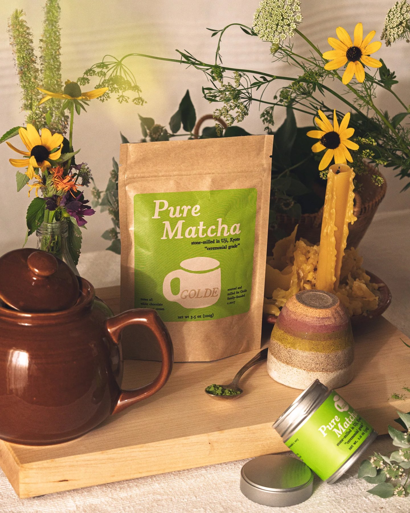 Tea set scene with Pure Matcha bag spoon flowers and open jar.