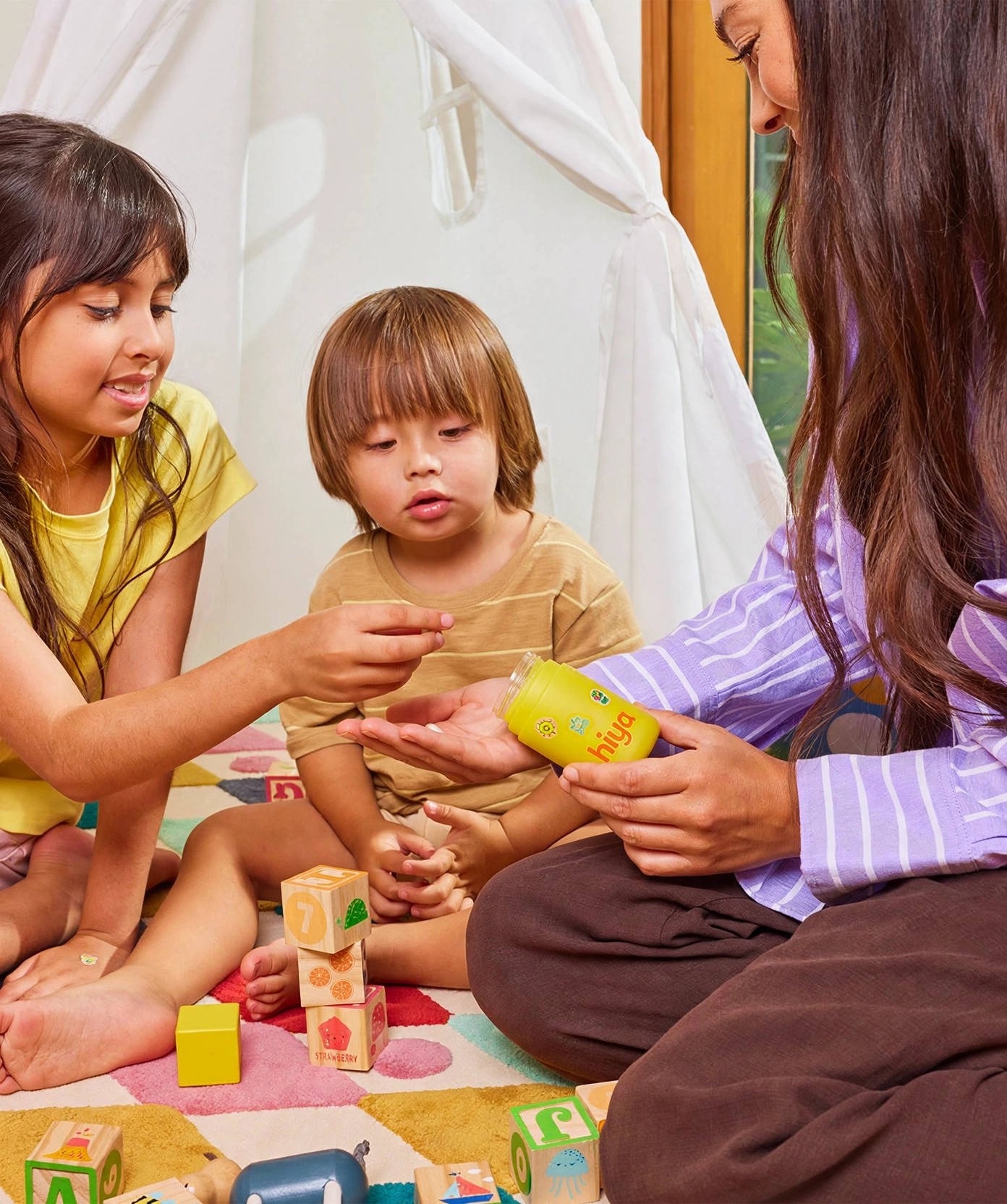 Two young kids receive a vitamin from a woman holding Hiya.
