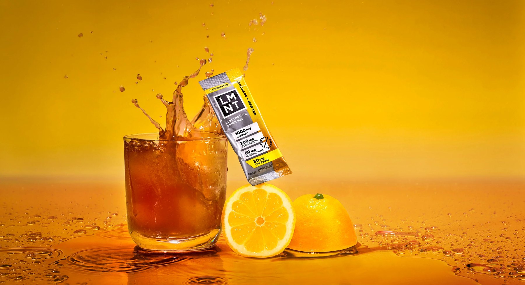 Iced tea splashing beside LMNT stick pack and sliced lemons.