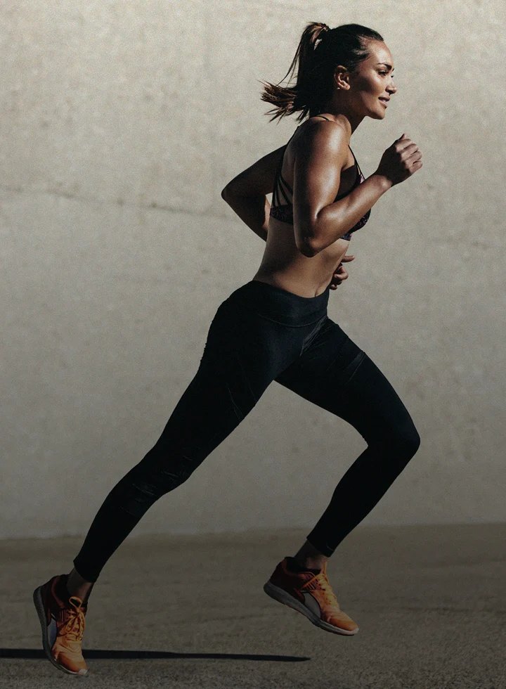 Woman in workout clothes running past a textured concrete wall.