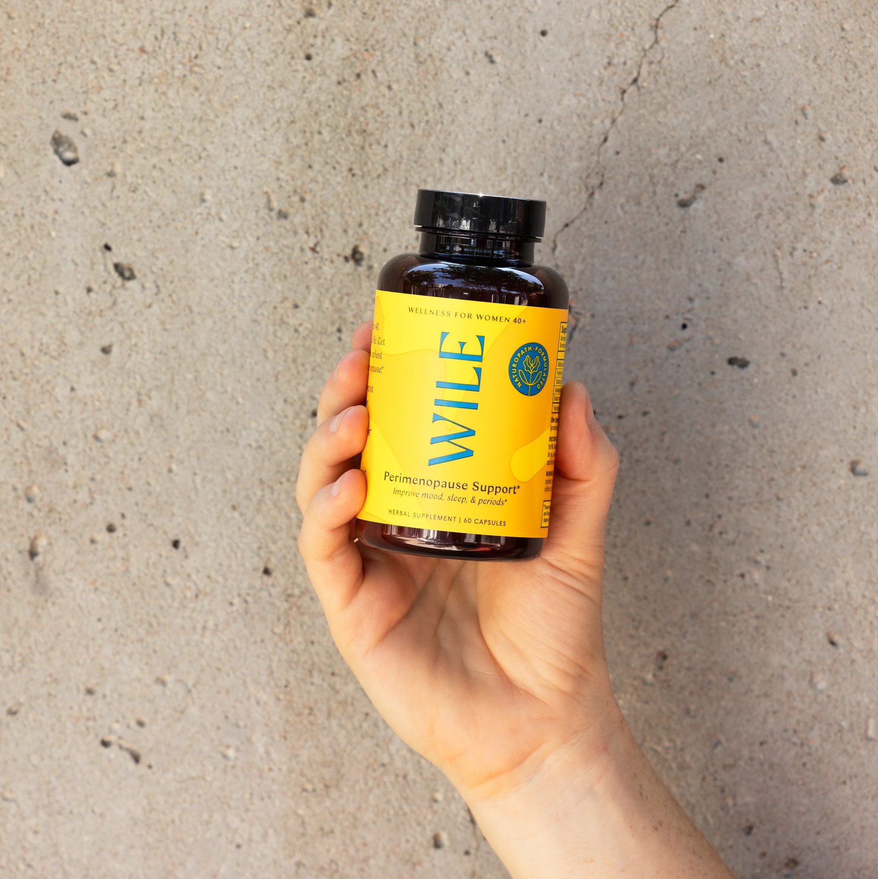A palm presents Wile Perimenopause Support bottle outdoors in daylight.