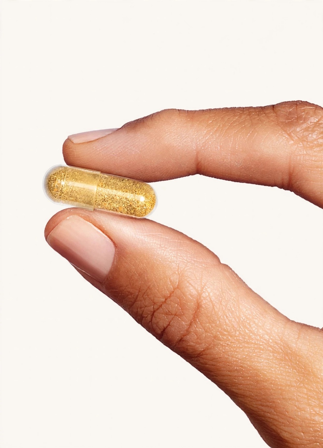 A hand presents a translucent capsule filled with golden powder.